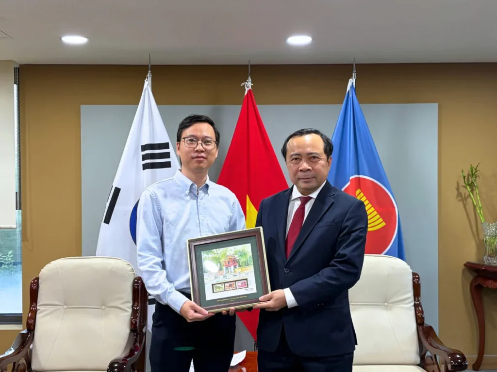 DEHA Global CEO Brian receives a framed painting from Vietnam's Minister of Science and Technology, Vu Hai Quan, in front of the Korean, Vietnamese and ASEAN flags.