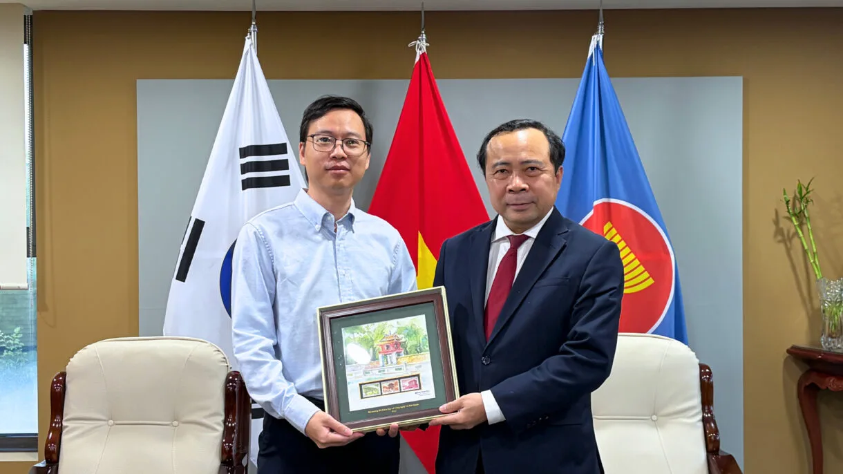 DEHA Global CEO Brian receives a framed painting from Vietnam's Minister of Science and Technology, Vu Hai Quan, in front of the Korean, Vietnamese and ASEAN flags.